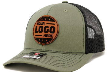 Loden/black Richardson 112 trucker hat with a round tan leather patch that reads “Your Logo Here” and a black mesh back.